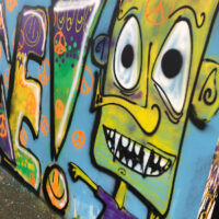 Ausschnitt der im letzten Jahr durch die Schüler*innen des Gymnasiums angebrachten Graffitis. Eine Figur mit gelbem Kopf und einem Peace-Zeichen auf der Stirn. (Foto: Robert Görne)