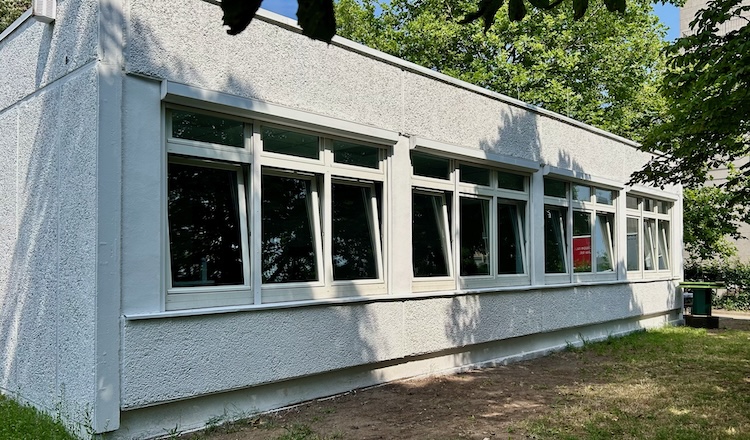 weißer Flachbau mit vier drei-flügeligen Fenstern