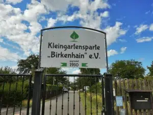 Ein Bild, das draußen, Tafel mit Text, Wolke, Himmel enthält. Auf der Tafel steht: Kleingartensparte "Birkenhain" e. V., gegründet 1910.
