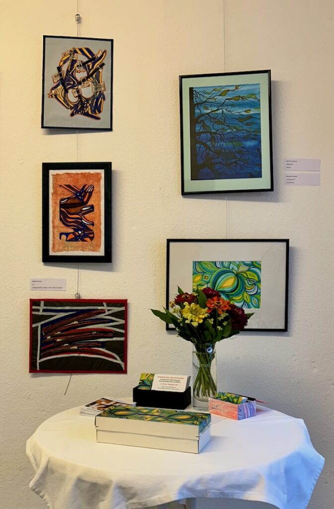 ein Tisch mit Blumen undverschiedenen Karten, im Hintergrund fünf verschieden Kunstwerke