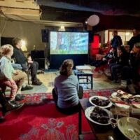 Menschen sitzen im Studio im Kreis und schauen auf einen Bildschirm mit der Videovorführung.