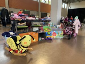 Stand auf einem Trödelmarkt mit Kinderkleidung davor eine große Biene als Schaukelpferd