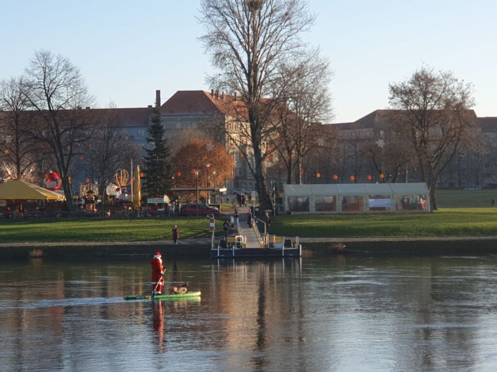 Ein Mann im Weihnachtsmannkostüm steht auf einem Steh-Paddelboot und lässt sich von der Flussströmung flussabwärts treiben.