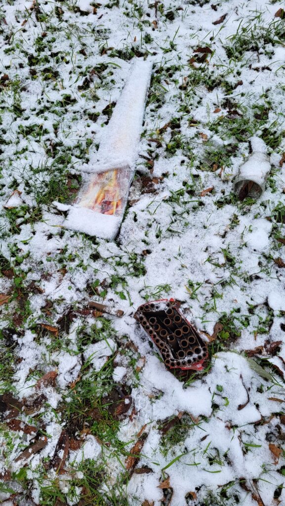 Überreste von Silvesterfeuerwerk liegen auf einer verschneiten Grünfläche.