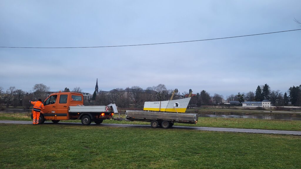 Ein Transportfahrzeug mit einem Anhänger. Auf dem Anhänger befindet sich ein Bauteil für einen Kinderspielplatz.