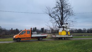 Ein Transportfahrzeug mit einem Anhänger. Auf dem Anhänger befindet sich ein Bauteil für einen Kinderspielplatz.