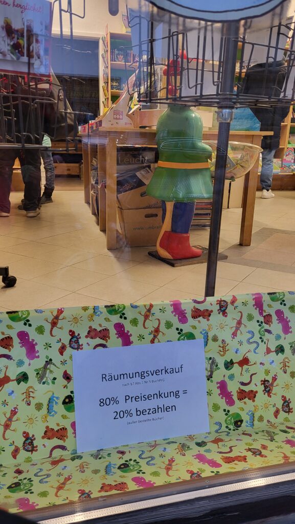 Blick in das Schaufenster eines Buchladens. Es ist ein Schild zu sehen auf dem Text steht: Räumungsverkauf - 80 % Preissenkung = 20 % bezahlen.