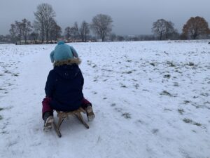 Kind mit blauer Mütze auf Schlitten im Winter